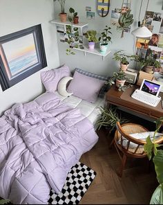 a bed with purple comforter sitting next to a laptop computer on top of a wooden desk