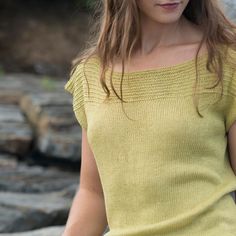 a woman in a yellow shirt is holding a cell phone and looking down at the ground