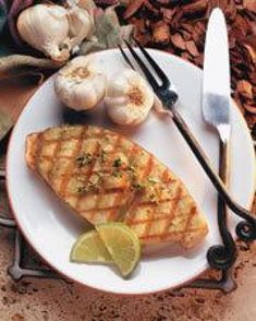 a white plate topped with fish next to garlic and lemon wedges on a table