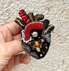 a hand holding a beaded heart brooch with red and black beads on it