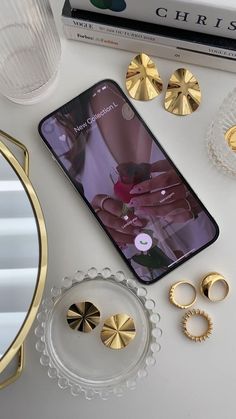 the phone is next to some gold rings and other accessories on top of a white table