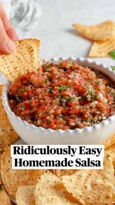 someone dipping salsa into a bowl with tortilla chips