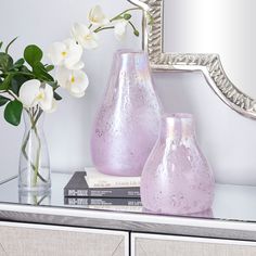 two vases with white flowers sit on a shelf next to a mirror and books