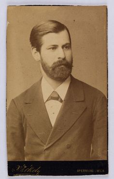 an old photo of a man with a beard wearing a suit and tie, standing in front of a white background