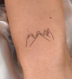 a small tattoo on the leg of a person with mountains in the background and hands holding each other