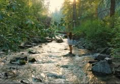 a woman standing in the middle of a river with her arms raised above her head