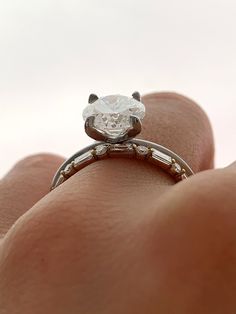 a person's hand holding a ring with a diamond in the middle and two diamonds on each side