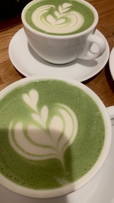 two cups of green tea with white designs on the top and bottom, sitting next to each other