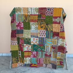 a multicolored patchwork blanket on a metal stand in front of a wall