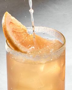 an orange slice is being poured into a glass filled with ice and lemon juice on a gray background