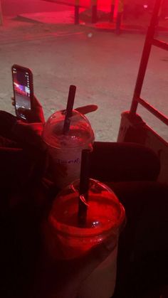 two drinks in plastic cups sitting next to each other with a cell phone on top