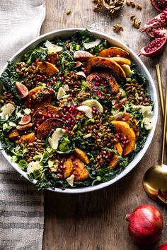 a bowl filled with salad next to two gold spoons and pomegranate