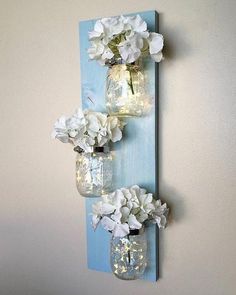 two mason jars with flowers are hanging on the wall