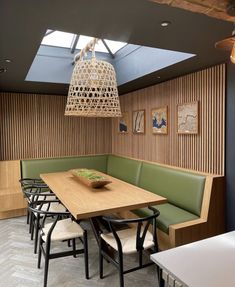 a wooden table sitting under a skylight in a room with green booths and chairs