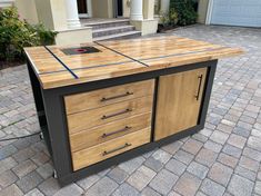 a kitchen island made out of wood and metal with drawers on the top, in front of a house