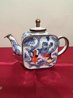 a blue and white teapot sitting on top of a red cloth covered tablecloth