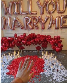 someone is reaching for some red hearts on the floor in front of a wall that says, will you marry me?