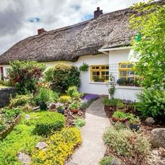 a white house with a thatched roof surrounded by greenery and flowers in the front yard