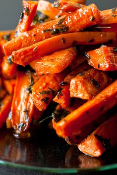 a glass plate filled with cooked carrots on top of a black tablecloth covered table