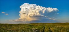 a large cloud is in the sky over a grassy field with a dirt road leading to it