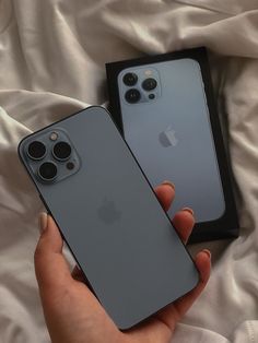 two iphones in their packaging being held by someone's hand on a bed