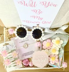 a gift box filled with pink and white flowers, sun glasses, cards, and other items