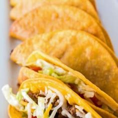 three tacos on a plate with shredded cheese and lettuce in the middle