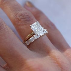 a woman's hand with a diamond ring on top of her finger and the other hand holding an engagement ring