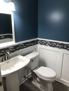 a white toilet sitting next to a sink in a bathroom under a mirror with blue walls