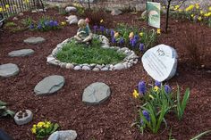 a garden with flowers, rocks and a plaque on the ground in front of it