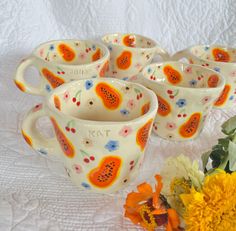 four ceramic mugs with designs on them next to a yellow flower bouquet and white quilt