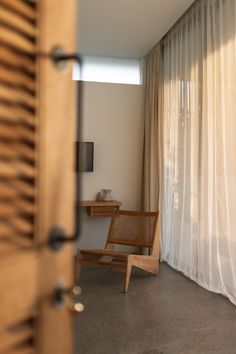 a wooden chair sitting in front of a window next to a white curtained wall