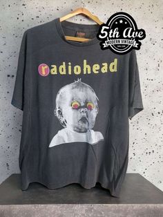 :his vintage-inspired Radiohead t shirt is made from 100% cotton, making it soft, breathable, and comfortable to wear. The black fabric is accented with a bold white print featuring the iconic Pablo Honey Tour logo, which showcases the band's name and tour details in a sleek, minimalist design. The shirt features a classic crew neck and short sleeves, making it a versatile option for any casual occasion. It is expertly crafted with a single stitch construction, creating a clean and streamlined look that is both durable and timeless. This technique involves using a single thread to sew the seams of the shirt, resulting in a smooth finish without any extra bulk or excess fabric. The Radiohead Pablo Honey Tour t shirt is a must-have for any true fan of the band or collector of vintage concert Washed Black Band Merch T-shirt With Graphic Print, Vintage Graphic Print T-shirt For Alternative Fashion, Vintage Short Sleeve T-shirt For Music Festivals, Acid Wash Alternative Style T-shirt With Screen Print, Retro Concert T-shirt With Logo Print, Retro Black T-shirt For Concert, Retro Logo Print T-shirt For Concert, Casual T-shirt For Music Festivals And Alternative Fashion, 90s Band Logo T-shirt For Music Festivals