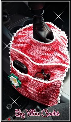 a red and white knitted bag with sunglasses in it sitting on top of a car steering wheel