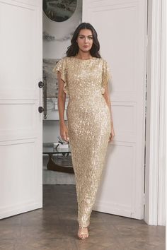 a woman standing in front of a door wearing a gold dress