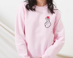 Korean Finger Love Symbol T-shirt Korean Finger Heart Cute KPop Tee K-pop Shirt Kpop Shirt Finger Heart Tee For him and for her ✅ FEATURES: 👉 Medium-heavy fabric blend: 50% cotton, 50% polyester (8.0 oz/yd² or 271.25 g/m²) 👉 Cozy feel, suitable for colder months 👉 Classic fit with a crew neckline for comfort and a clean-cut style 👉 Double-needle stitching for enhanced durability at shoulder, armhole, neck, waistband, and cuff seams 👉 Gray, pearlized tear-away label to eliminate itchiness 👉 Made with 100% ethically grown US cotton 👉 OEKO-TEX-certified dyes used for low environmental impact 👉 Fabric blends for Heather Sport colors: 60% polyester, 40% cotton 🌸 THANKS FOR VISITING OUR SHOP 🌸 Kpop Long Sleeve T-shirt With Letter Print, Pink Long Sleeve T-shirt With Heart Graphic, Cute Long Sleeve T-shirt With Heart Print, Pink Kpop Tops With Graphic Print, Pink Kpop Graphic Print Top, Pink K-pop Style Top With Graphic Print, Long Sleeve T-shirt With Heart Graphic For Gift, Cute Long Sleeve T-shirt As Gift, Trendy Pink T-shirt For Valentine's Day