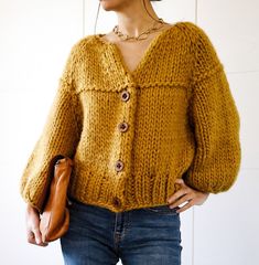 a woman wearing a mustard colored cardigan sweater and headphones stands in front of a white wall