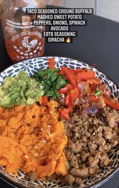 a plate with meat, vegetables and sauces on it next to a bottle of booze