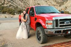 a bride and groom standing next to a red truck