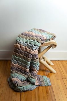 a crocheted blanket sitting on top of a wooden stool next to a wall