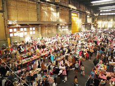 a large room filled with lots of people standing around and looking at items on tables