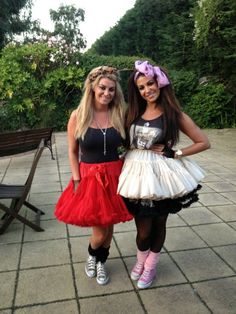 two young women dressed in costumes posing for the camera on a brick walkway with trees and bushes behind them