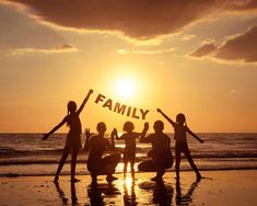 four people are standing on the beach with their arms in the air as the sun sets