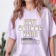 Our "Back To School Shirt" is a fun blend of retro aesthetics and humorous anticipation for the upcoming academic year. With its vintage distressed graphic, this retro shirt proudly displays the phrase "New School Year" in bold, eye-catching lettering. Adding a playful twist to the design, the shirt also features the phrase "Loading..." below, capturing the excitement and anticipation that comes with the first day of school. Perfect for teachers and students alike, this funny T-shirt is a must-h Retro School T-shirt With Text Print, Retro Text Print T-shirt For School, Retro Relaxed Fit Tops For School, Trendy School T-shirt With Slogan, Retro Crew Neck T-shirt For Back To School, Back To School Graphic Tee Shirt With Text Print, Back To School Graphic Tee With Text Print, Retro Letter Print T-shirt For School, Back To School Tops With Funny Text