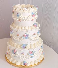 a three tiered white wedding cake with flowers on the top and sides, sitting on a table