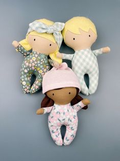 three dolls are laying next to each other on a gray background, one is wearing a pink hat