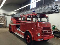 an old red fire truck parked in a garage with ladders on it's roof