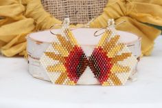 a pair of beaded earrings sitting on top of a white table next to a yellow cloth