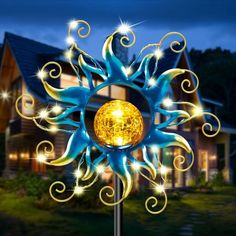 a blue and yellow sunflower stake with lights on it's face in front of a house