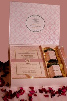 an open box containing three bottles of wine and rose petals on a table with pink wallpaper